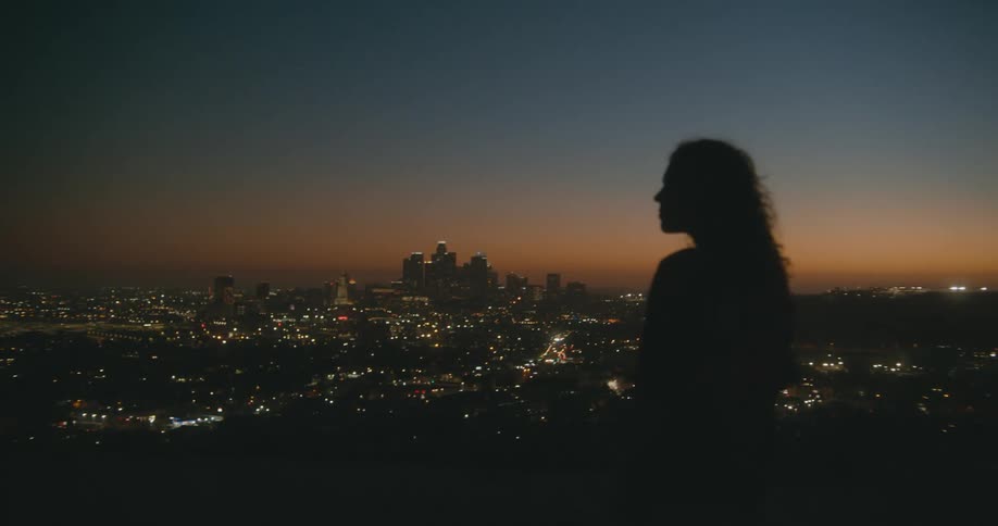 A woman stands and looks down at the city below her vantage point