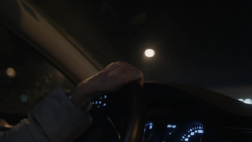 Driver wearing coat steers car along streets passing businesses at night