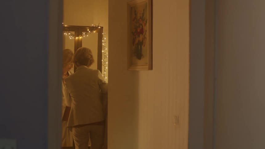 Woman removes coat while looking at herself in mirror decorated with twinkling lights