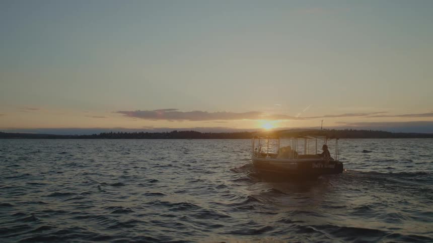 A few people are on a boat near the coast as the sun comes up