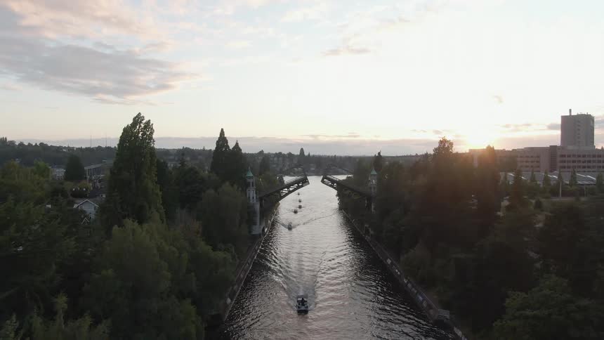Boats travel along a waterway beneath a drawbridge in the evening