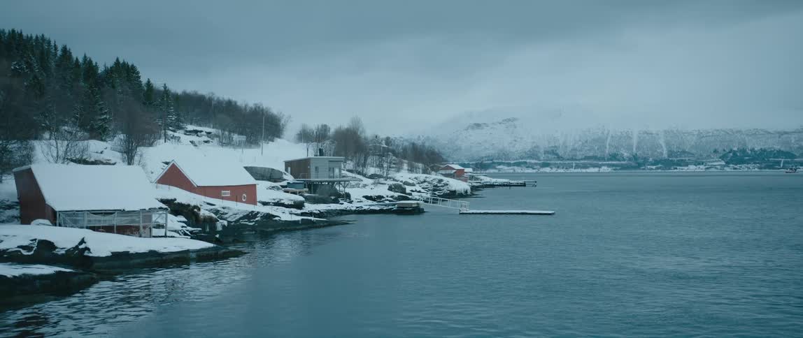Snow covered homes and docks on the side of a lake with a mountain on the horizon