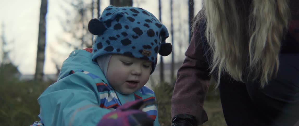 A woman hands a branch to a baby who digs in the dirt with it