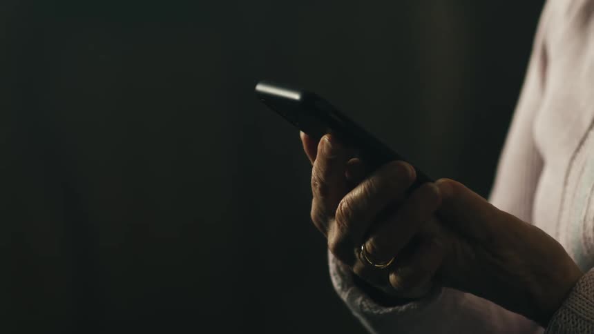An elderly woman is holding a cell phone with both hands