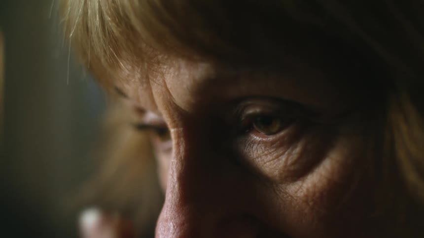 A woman removes her glasses and rubs the corners of her eyes with her hand