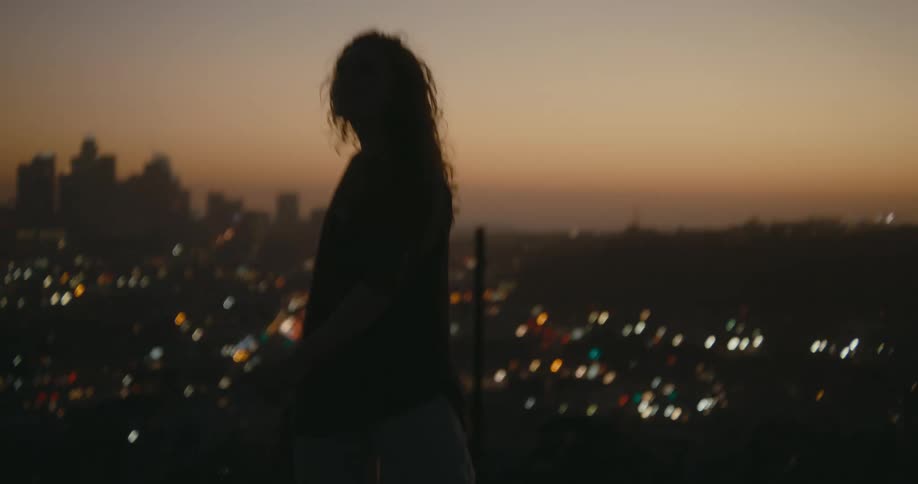 Woman with curly hair and shirt dancing against the skyline is silhouetted agains the red sky