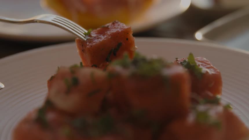 A fork picks up a piece of raw fish from a plate