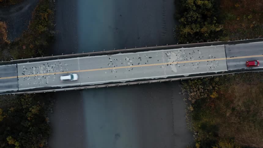 Vehicles cross on a bridge over water to the land