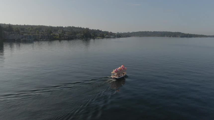 A boat decorated with balloons travels across a lake during the day