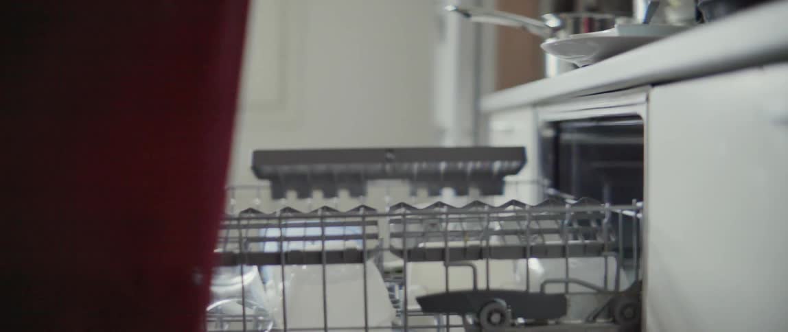 A woman removes clean glassware and plates from a dishwasher in a modern kitchen.