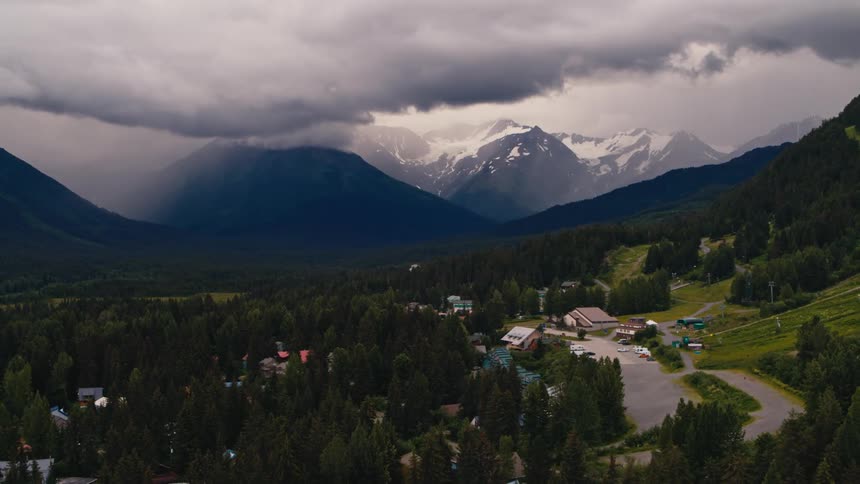Thick clouds loom over a small town in a mountain valley during the day