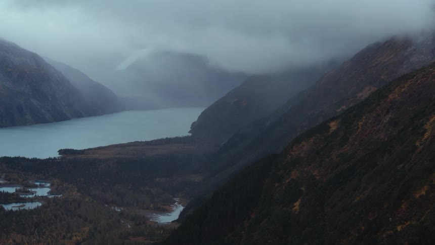 A mountain slope leading towards a river covering the floor of a mountain valley on a cloudy day