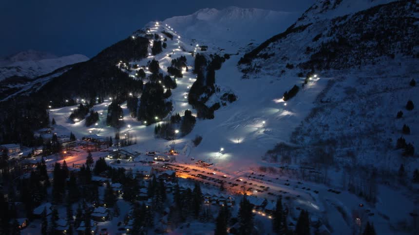 Traffic moves around brightly lit town in valley during winter at night