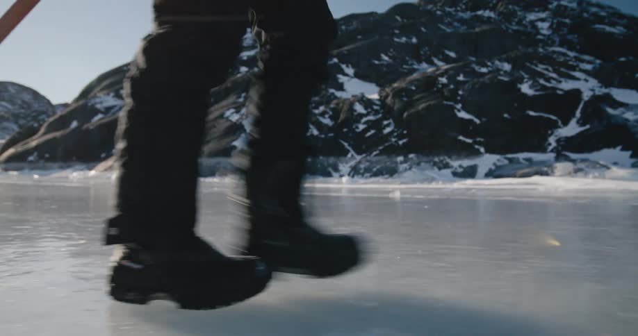 A man uses a walking stick as he crosses over ice near a mountain