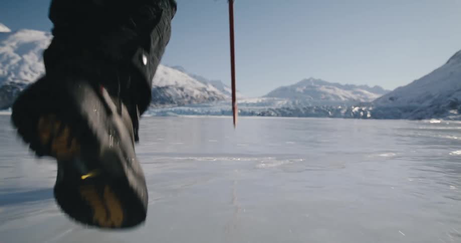 A person trekking across a frozen lake using a pole to tap ahead