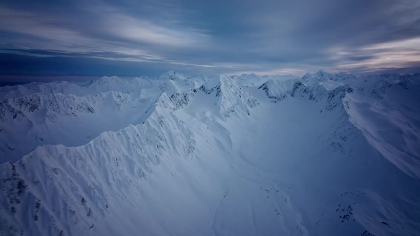 Low lying clouds move quickly across top of snow covered mountains under a red tinted sky