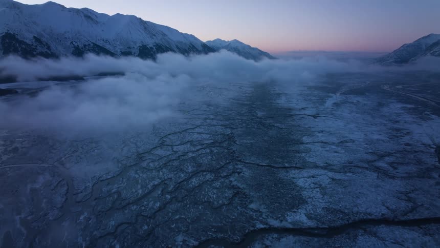 Fog moves across an icy surface in a valley between mountains