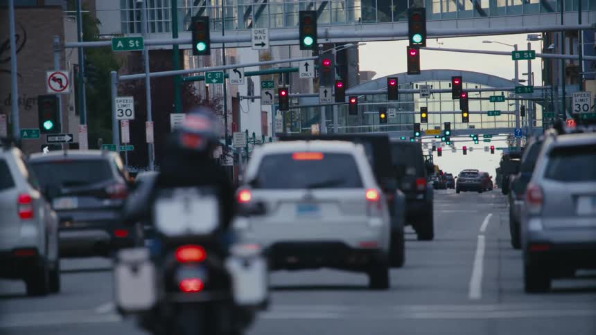 Traffic flows down city street as pedestrians cross through intersection