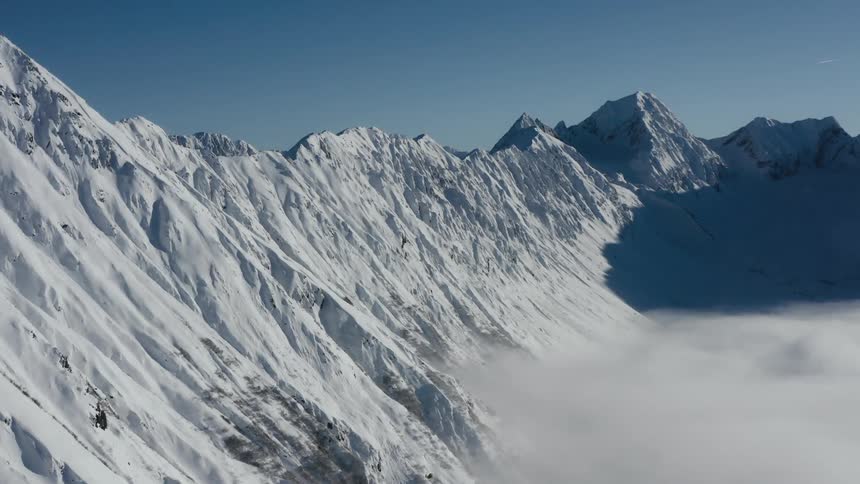 A snow covered mountain ridge with peaks high in a clear sky