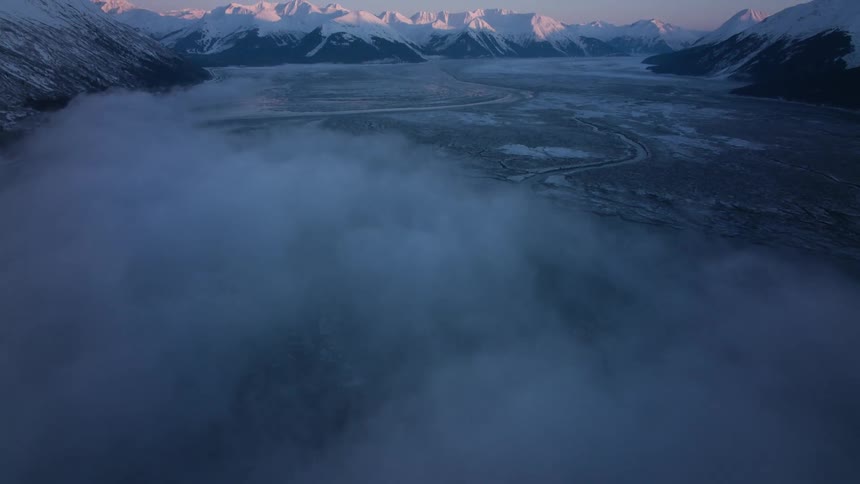 Winding streams cross a frozen valley between mountains during the day
