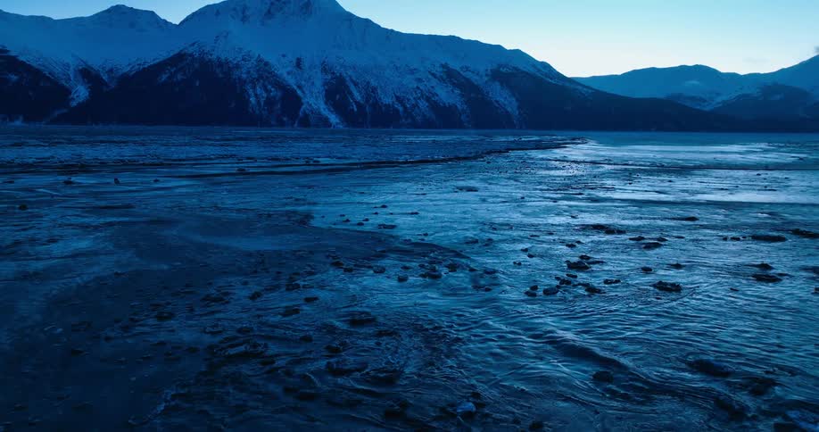 Waves ripple in a lake below a snow capped mountain
