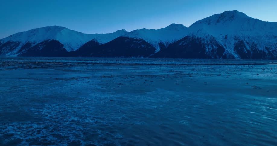Snow capped mountains on shore with water flowing past