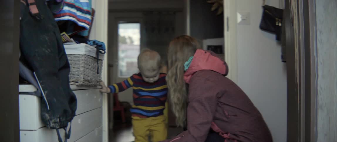 A woman assists a young toddler in removing his socks after coming inside from outdoors.