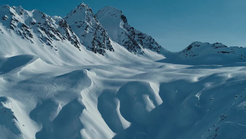 A snow covered mountain ridge with peaks high in a clear sky