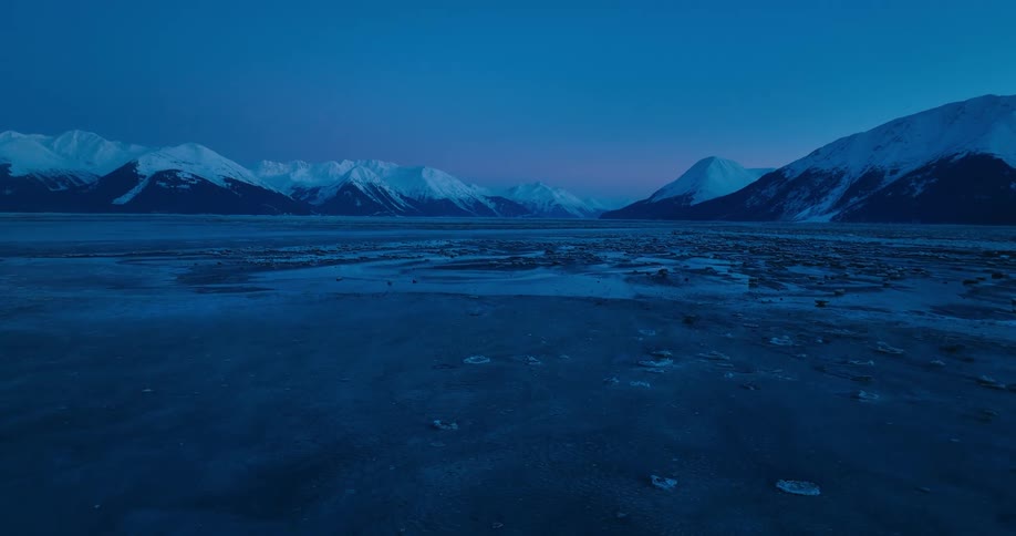 Water filled with ice moves ashore near a snowy mountain range