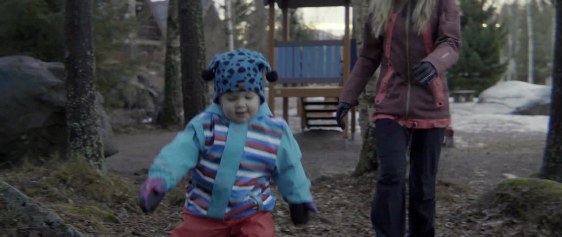 A woman walks after a young child playing outdoors in a snowy winter playground.
