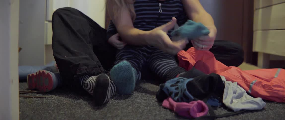 A woman sitting on the floor helps a child put on socks