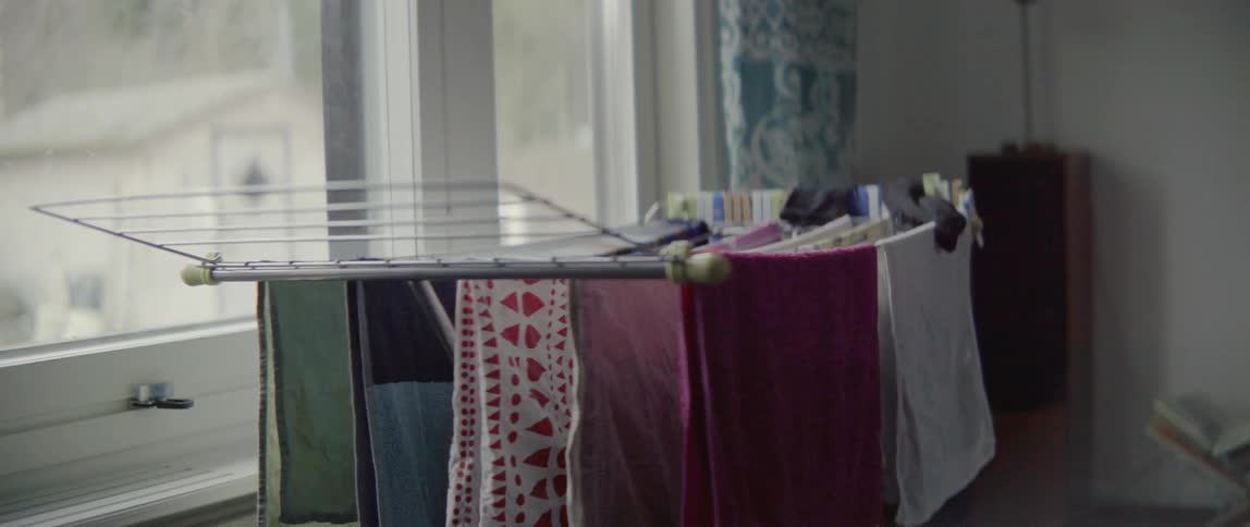A woman carefully hangs freshly washed clothes on a hanger in her home.
