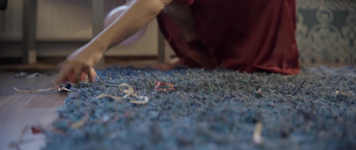 A woman reaches down to clear colorful party decorations and debris from a rug.