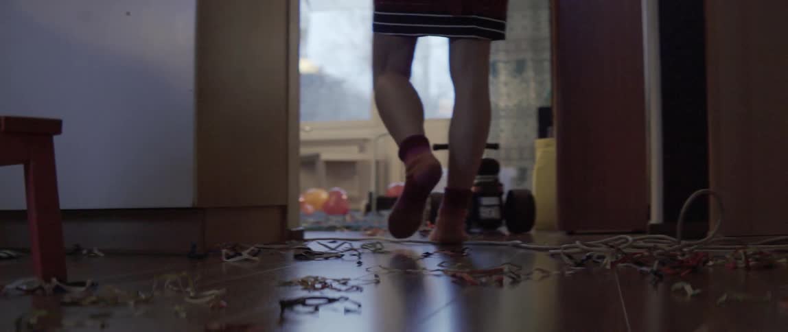 Person walking through a messy living space littered with colorful paper scraps and balloons.