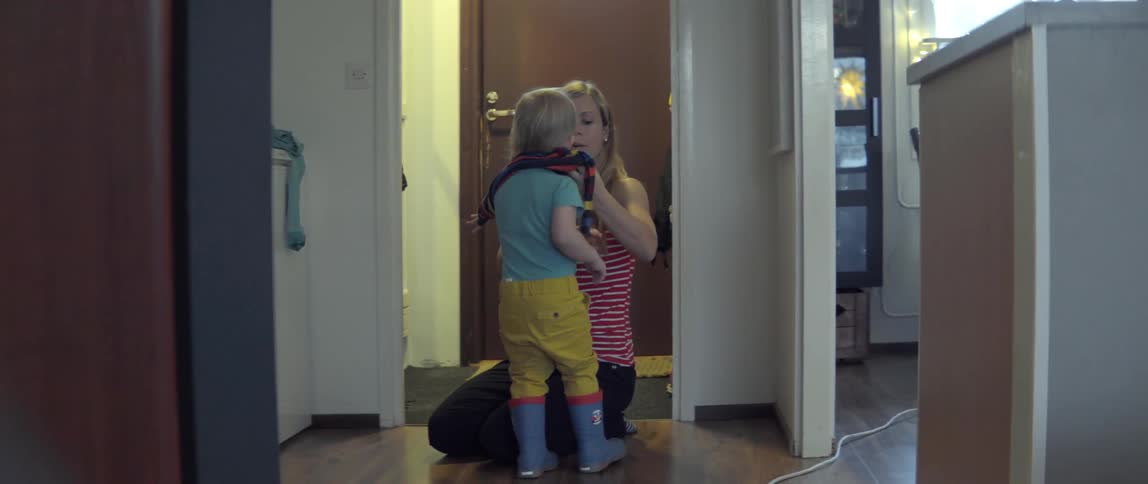 A woman helps a young toddler put on a warm sweater inside a modern home.