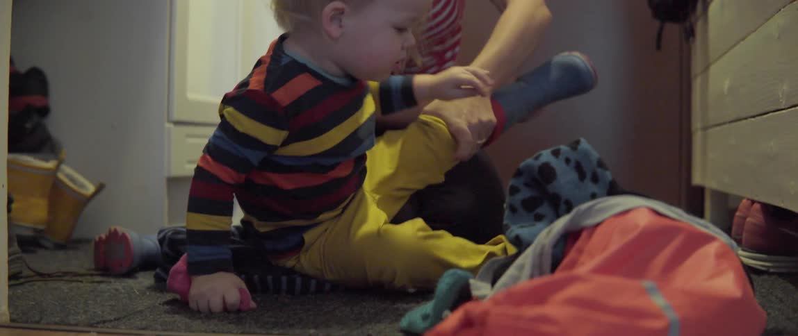 A woman assists a young toddler in removing his winter boots after coming indoors.