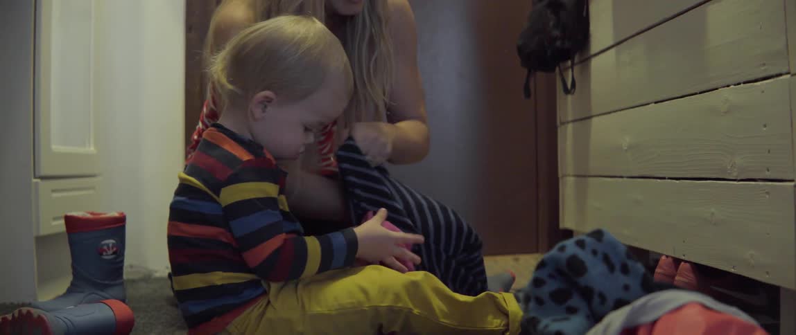 A woman helps a toddler get dressed by putting on a warm striped sweater.
