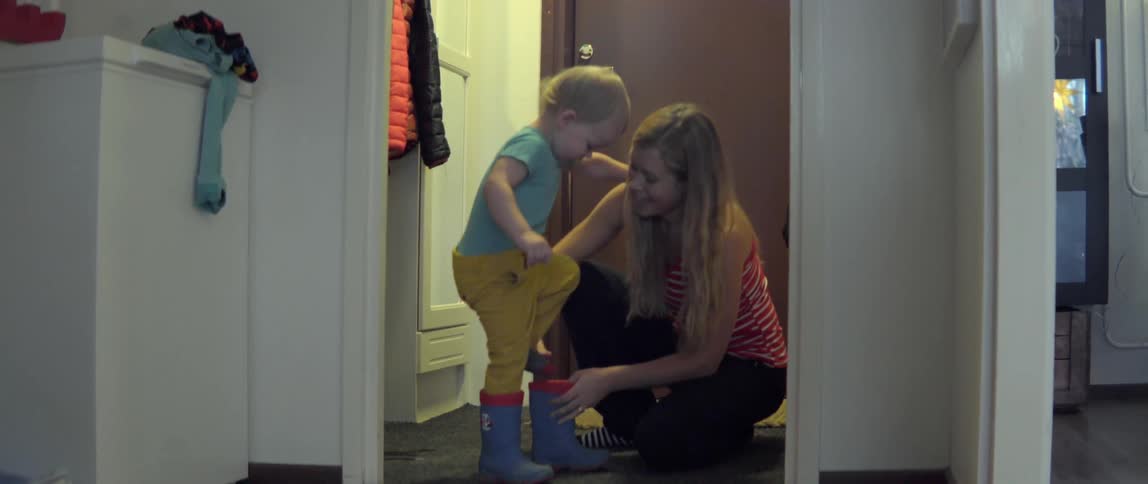 Young woman helping a small child prepare for a walk by putting on boots.
