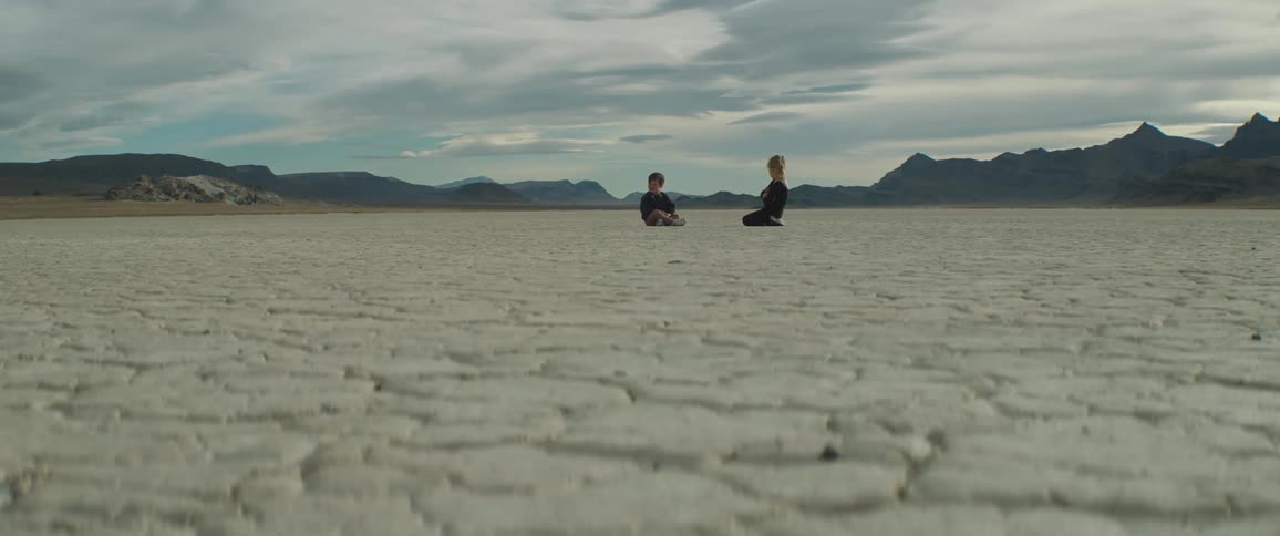 A boy and girl sit in a desert area