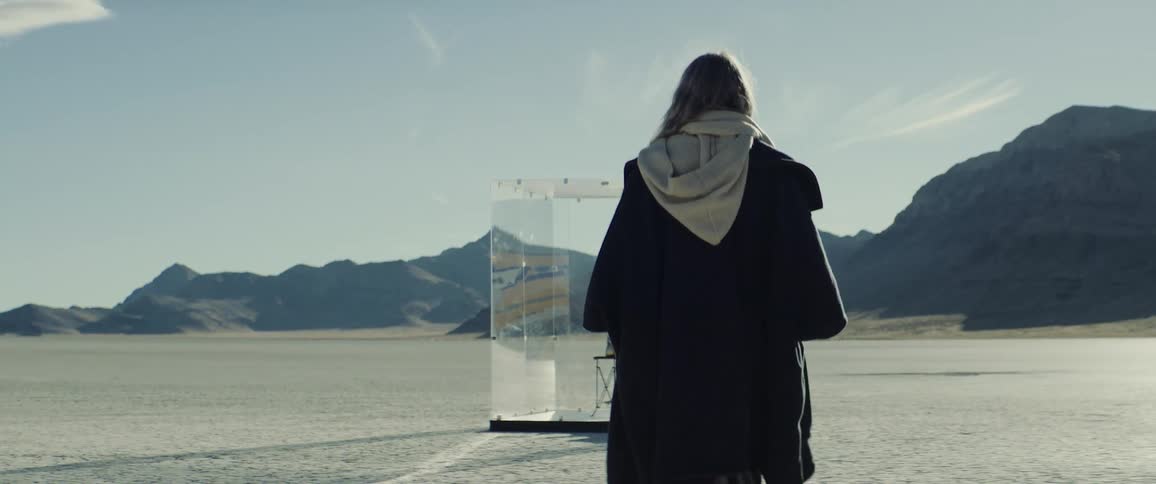 A woman in a desert walks towards a glass enclosure