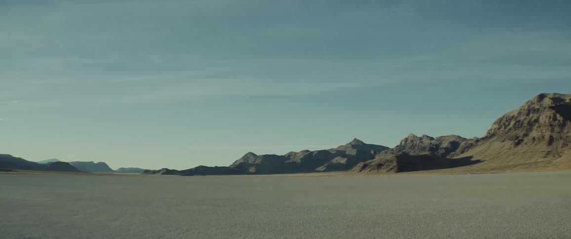 Desert stretches to misty mountains on the horizon under a cloudy sky
