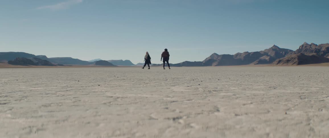 Two people walk by each other in the desert