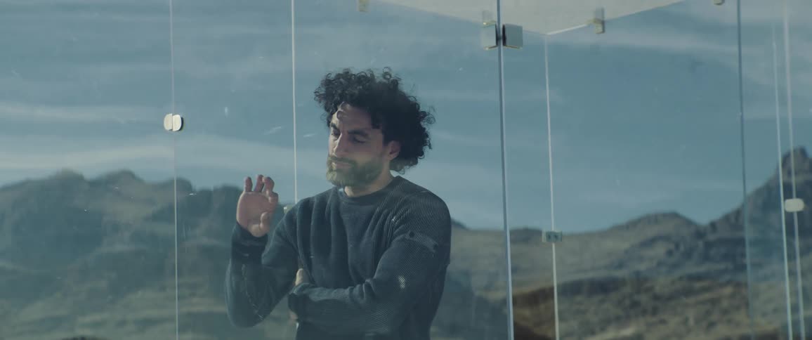 A man in a glass enclosure puts his hand up to the glass as he stands still