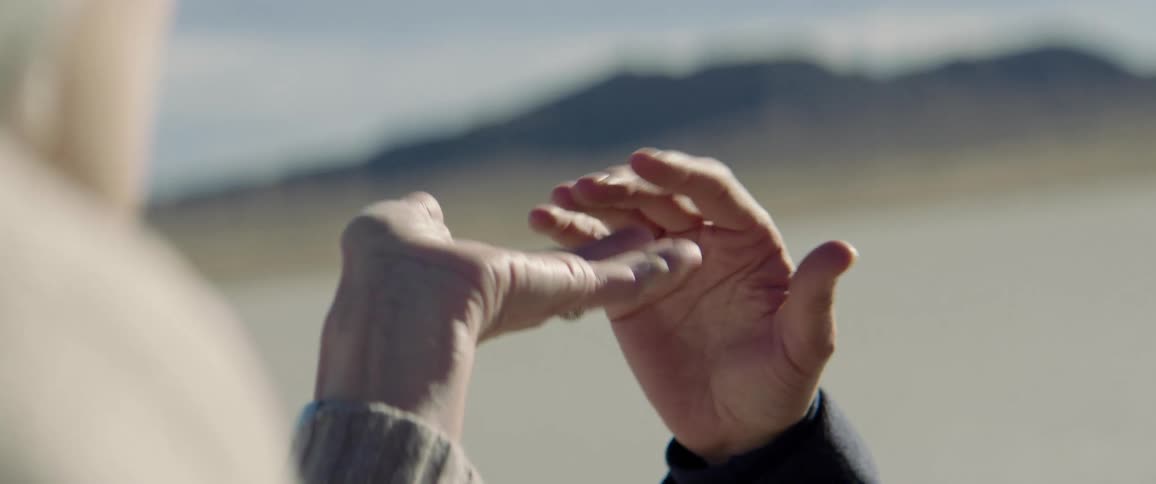 A man and a woman wave their hands and embrace while standing in the desert