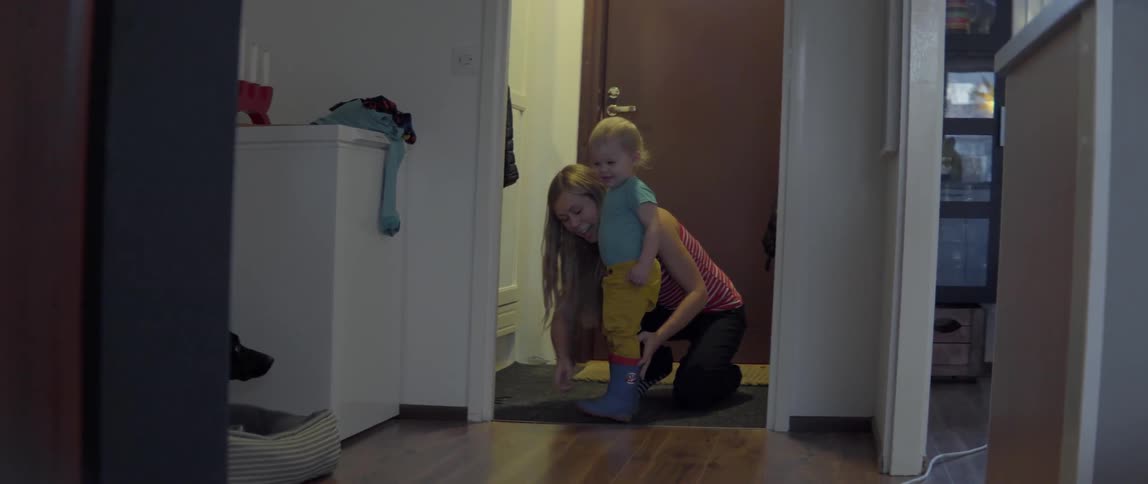 Young woman helping a toddler prepare for a walk by putting on his shoes.