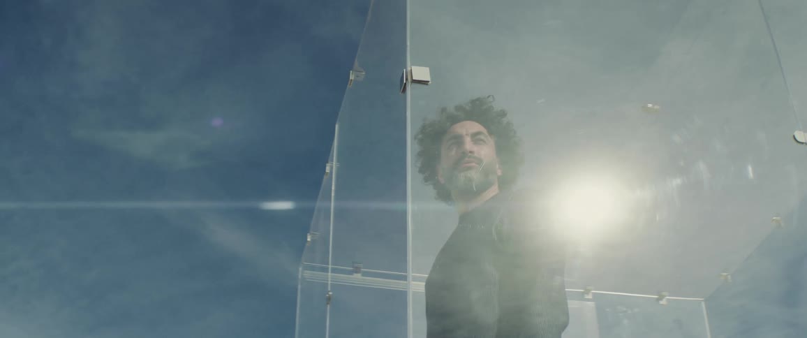 Man stands in plexiglas enclosure looking around on sunny day