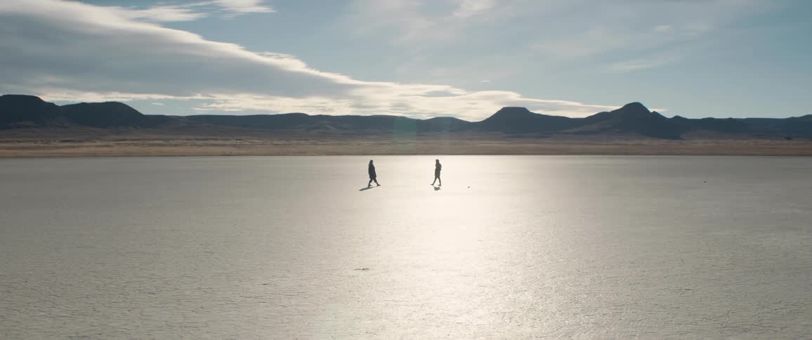 Two people face on another holding hands and then let go and they each step backwards and walk away from one another