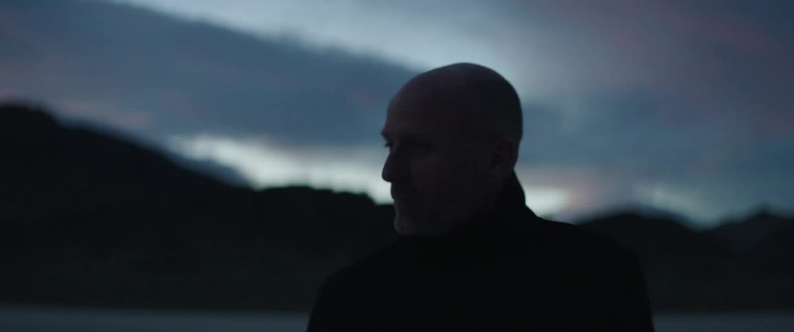 Man with black coat looks around and walks away in the desert at dusk