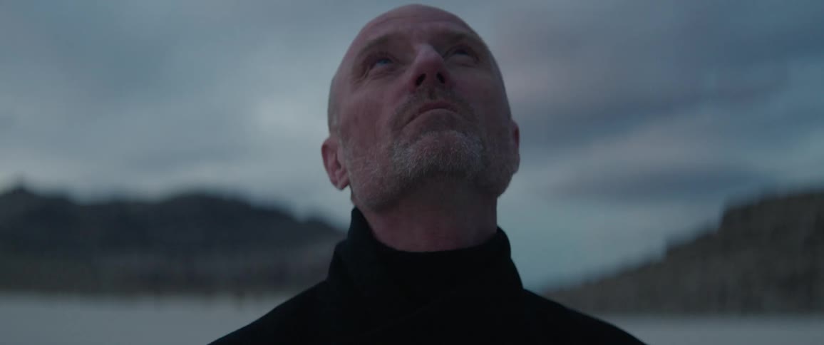 Middle aged man with black turtlneck sweater looks around in the desert