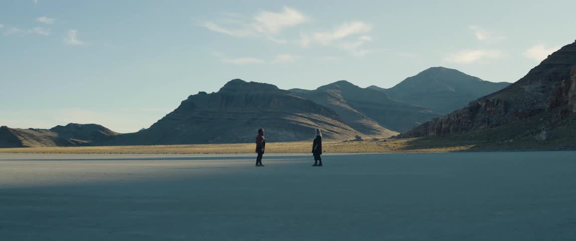 A man and woman walk away while facing each other in the desert